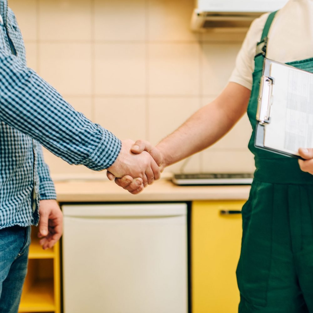 Repairman in uniform and customer shake hands, handyman. Professional worker makes repairs around the house, home repairing service